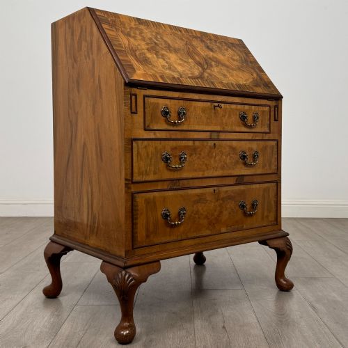 fig 8. An Edwardian burr walnut writing bureau featuring a sloping fall front, three drawers with decorative brass handles, and cabriole legs.