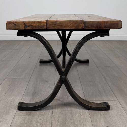 fig 1. A low rectangular coffee table featuring a thick hardwood plank top set upon a dark curved iron X-frame base.