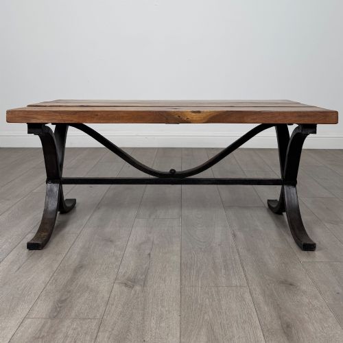 fig 3. A low rectangular coffee table featuring a thick hardwood plank top set upon a dark curved iron X-frame base.