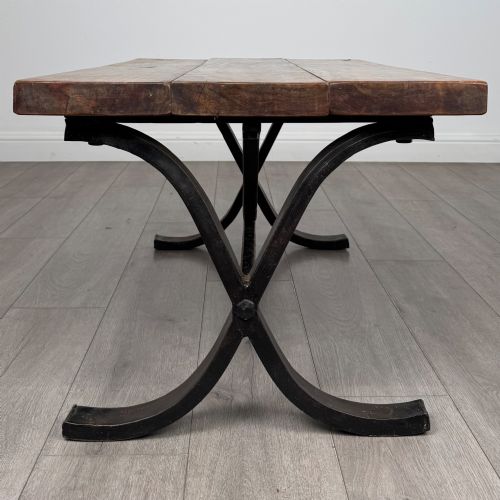 fig 5. A low rectangular coffee table featuring a thick hardwood plank top set upon a dark curved iron X-frame base.