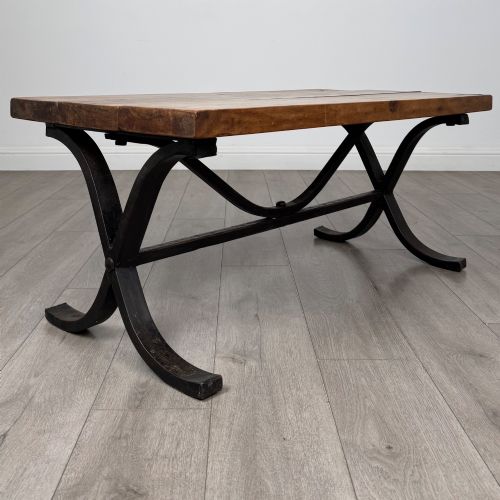 fig 6. A low rectangular coffee table featuring a thick hardwood plank top set upon a dark curved iron X-frame base.