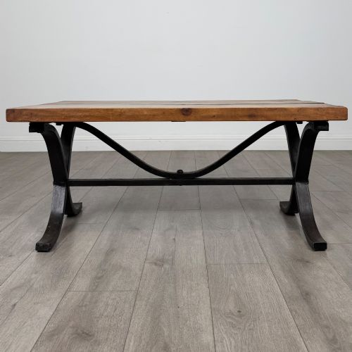 fig 7. A low rectangular coffee table featuring a thick hardwood plank top set upon a dark curved iron X-frame base.