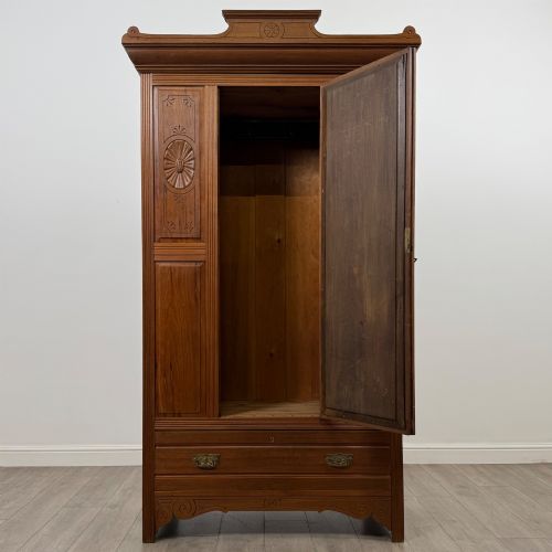 fig 1. An Edwardian walnut wardrobe featuring a central mirrored door flanked by carved timber panels above a single base drawer.