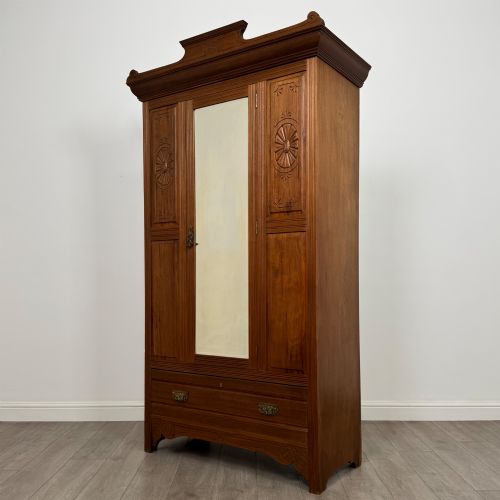 fig 2. An Edwardian walnut wardrobe featuring a central mirrored door flanked by carved timber panels above a single base drawer.