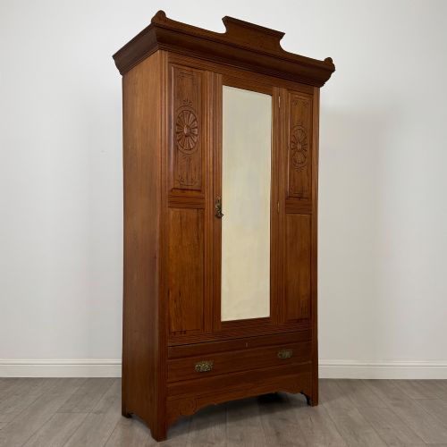 fig 8. An Edwardian walnut wardrobe featuring a central mirrored door flanked by carved timber panels above a single base drawer.