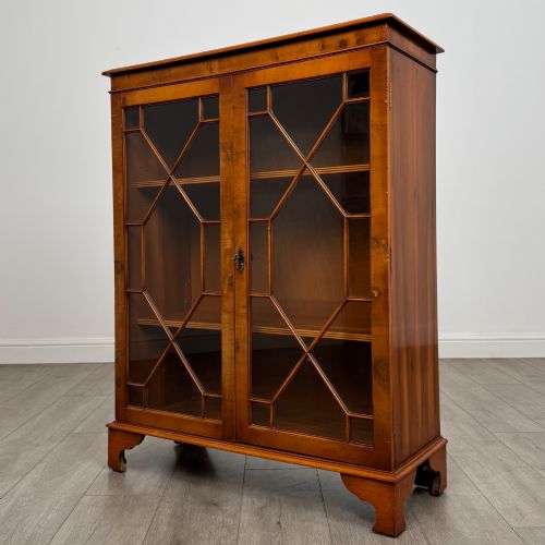 fig 3. An antique yew wood display cabinet featuring two astragal glazed doors with geometric glazing bars, housing books on internal shelves, and resting on bracket feet.