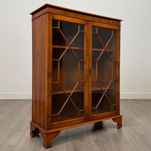 fig 9. An antique yew wood display cabinet featuring two astragal glazed doors with geometric glazing bars, housing books on internal shelves, and resting on bracket feet.
