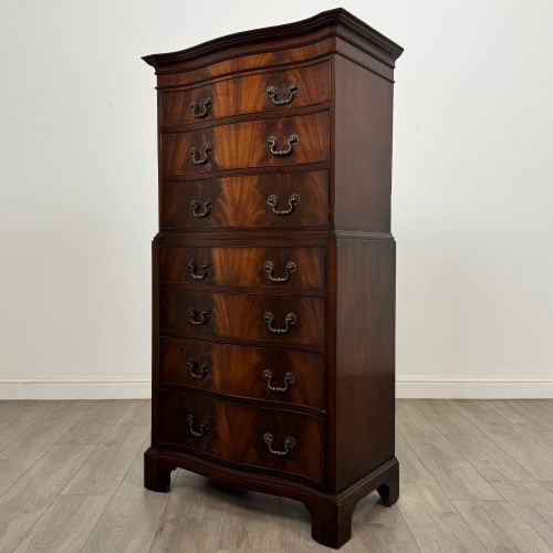fig 1. A tall 20th-century mahogany serpentine chest of drawers featuring seven graduated drawers with brass handles and bracket feet.