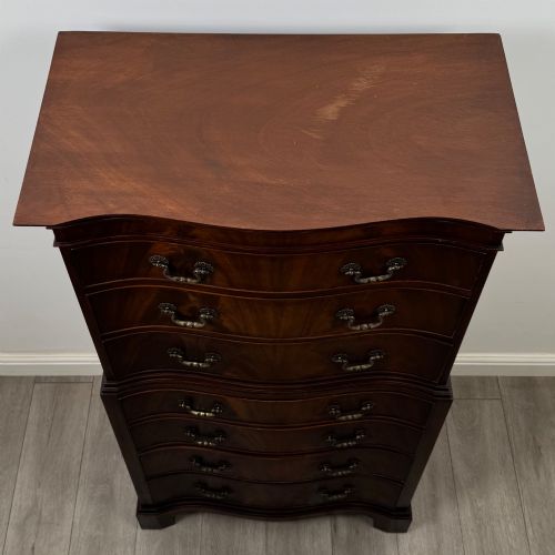 fig 8. A tall 20th-century mahogany serpentine chest of drawers featuring seven graduated drawers with brass handles and bracket feet.