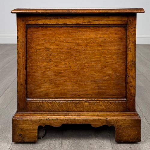 fig 3. A low two-drawer oak chest featuring raised panel fronts, decorative brass drop handles, and bracket feet in a warm brown finish.