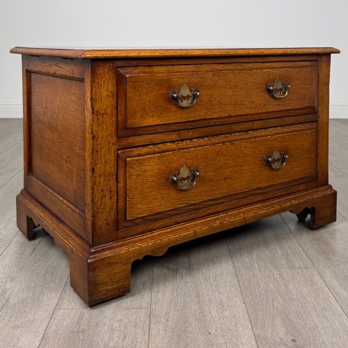 fig 8. A low two-drawer oak chest featuring raised panel fronts, decorative brass drop handles, and bracket feet in a warm brown finish.