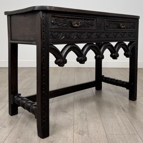 fig 7. A dark oak 19th-century side table featuring floral relief carvings on two drawer fronts, a row of carved cusped arches along the lower apron, and turned side stretchers.