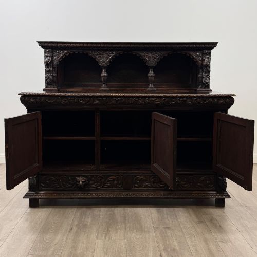 fig 1. A dark oak 19th-century sideboard featuring deep relief carvings of Green Man mythical faces, foliate motifs, lion masks, and an arched upper gallery shelf.
