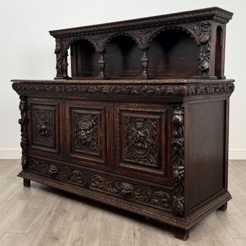 fig 2. A dark oak 19th-century sideboard featuring deep relief carvings of Green Man mythical faces, foliate motifs, lion masks, and an arched upper gallery shelf.