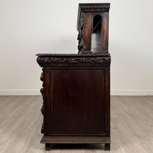 fig 3. A dark oak 19th-century sideboard featuring deep relief carvings of Green Man mythical faces, foliate motifs, lion masks, and an arched upper gallery shelf.