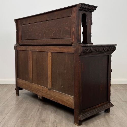 fig 6. A dark oak 19th-century sideboard featuring deep relief carvings of Green Man mythical faces, foliate motifs, lion masks, and an arched upper gallery shelf.