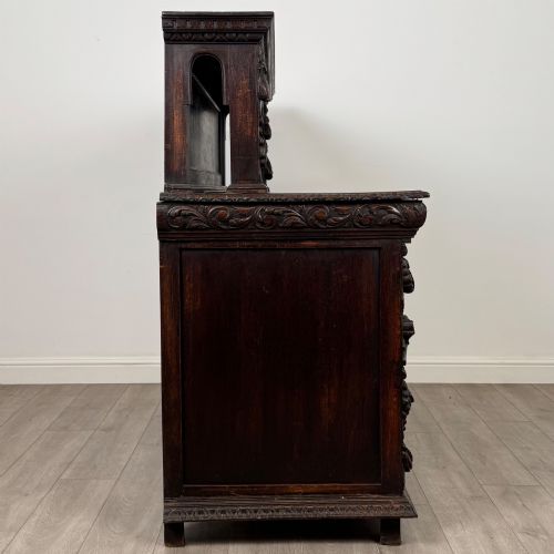 fig 7. A dark oak 19th-century sideboard featuring deep relief carvings of Green Man mythical faces, foliate motifs, lion masks, and an arched upper gallery shelf.