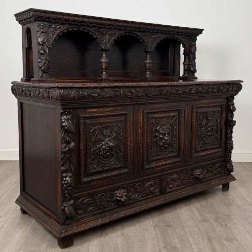 fig 8. A dark oak 19th-century sideboard featuring deep relief carvings of Green Man mythical faces, foliate motifs, lion masks, and an arched upper gallery shelf.