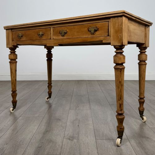 fig 1. A 19th-century Victorian pine writing table featuring two drawers with brass handles, turned wooden legs, and ceramic castors.