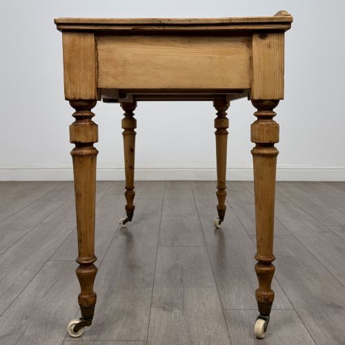 fig 2. A 19th-century Victorian pine writing table featuring two drawers with brass handles, turned wooden legs, and ceramic castors.