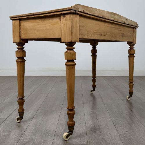fig 3. A 19th-century Victorian pine writing table featuring two drawers with brass handles, turned wooden legs, and ceramic castors.