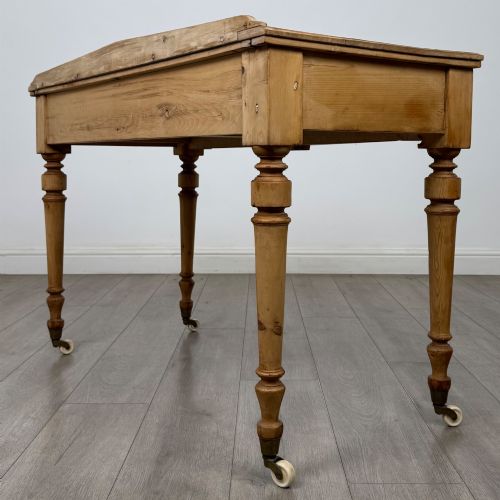 fig 5. A 19th-century Victorian pine writing table featuring two drawers with brass handles, turned wooden legs, and ceramic castors.