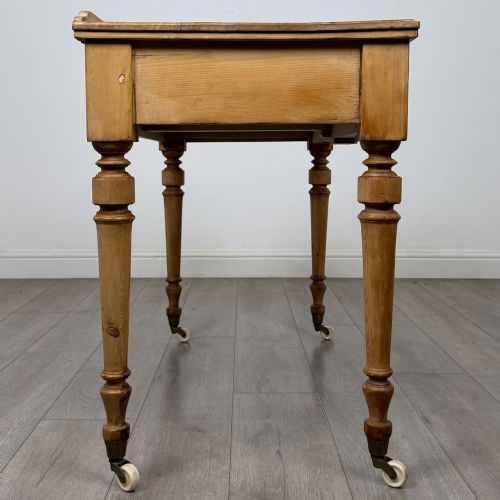 fig 6. A 19th-century Victorian pine writing table featuring two drawers with brass handles, turned wooden legs, and ceramic castors.