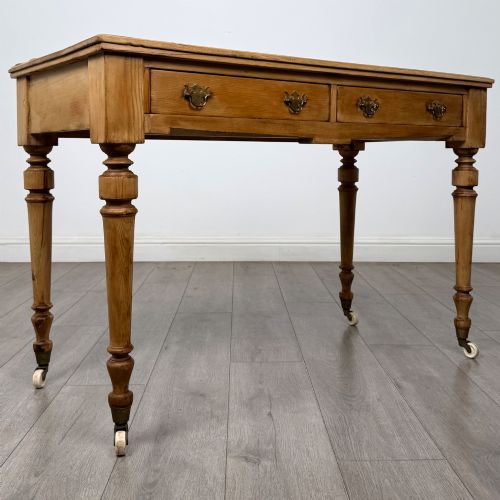 fig 7. A 19th-century Victorian pine writing table featuring two drawers with brass handles, turned wooden legs, and ceramic castors.