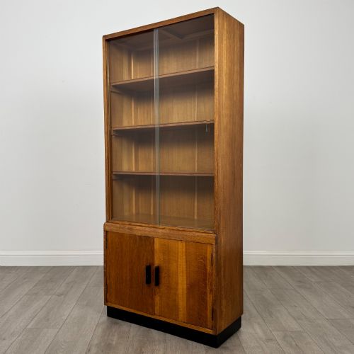 fig 3. A tall vintage golden oak display cabinet featuring glazed sliding doors on top and a two-door cupboard base.