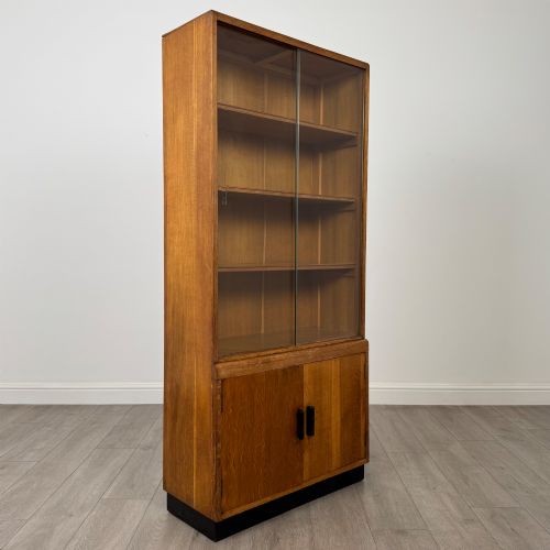 fig 9. A tall vintage golden oak display cabinet featuring glazed sliding doors on top and a two-door cupboard base.