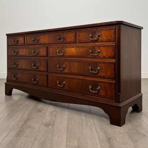 fig 1. A wide 20th-century mahogany chest of drawers featuring multiple drawer tiers with flame mahogany veneer and decorative brass handles.