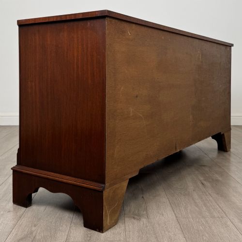fig 3. A wide 20th-century mahogany chest of drawers featuring multiple drawer tiers with flame mahogany veneer and decorative brass handles.