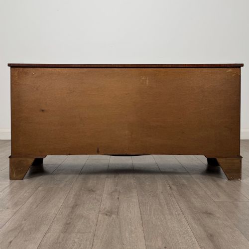 fig 4. A wide 20th-century mahogany chest of drawers featuring multiple drawer tiers with flame mahogany veneer and decorative brass handles.
