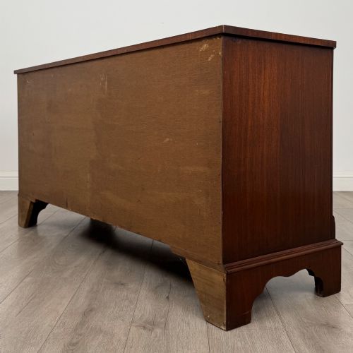fig 5. A wide 20th-century mahogany chest of drawers featuring multiple drawer tiers with flame mahogany veneer and decorative brass handles.