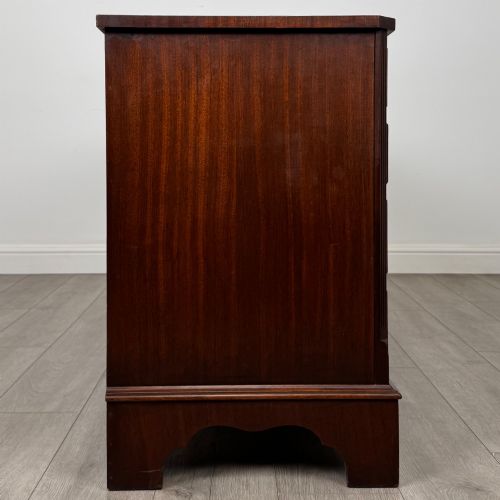 fig 6. A wide 20th-century mahogany chest of drawers featuring multiple drawer tiers with flame mahogany veneer and decorative brass handles.