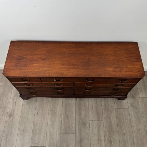 fig 8. A wide 20th-century mahogany chest of drawers featuring multiple drawer tiers with flame mahogany veneer and decorative brass handles.