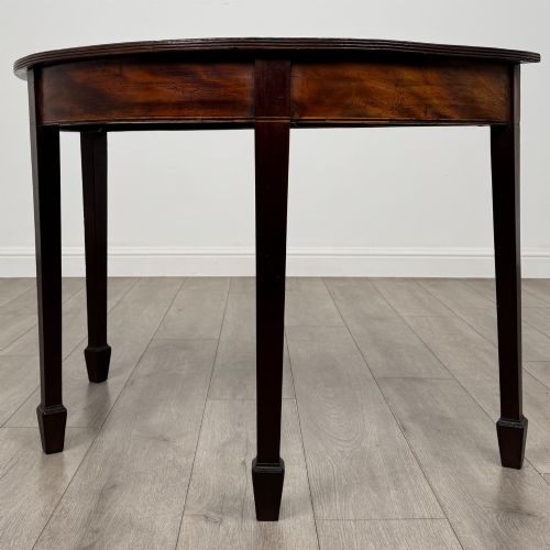 fig 1. A nineteenth-century mahogany demi-lune side table featuring a semi-circular top, a veneered apron, and four square tapered legs ending in spade feet.