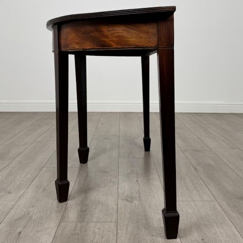 fig 2. A nineteenth-century mahogany demi-lune side table featuring a semi-circular top, a veneered apron, and four square tapered legs ending in spade feet.