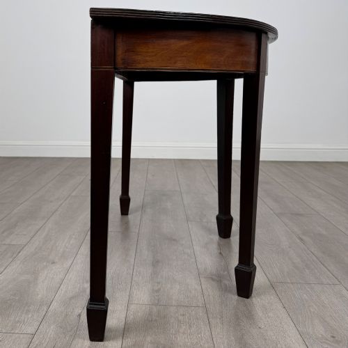fig 4. A nineteenth-century mahogany demi-lune side table featuring a semi-circular top, a veneered apron, and four square tapered legs ending in spade feet.