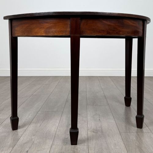 fig 5. A nineteenth-century mahogany demi-lune side table featuring a semi-circular top, a veneered apron, and four square tapered legs ending in spade feet.