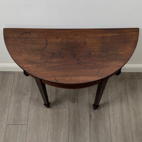 fig 6. A nineteenth-century mahogany demi-lune side table featuring a semi-circular top, a veneered apron, and four square tapered legs ending in spade feet.