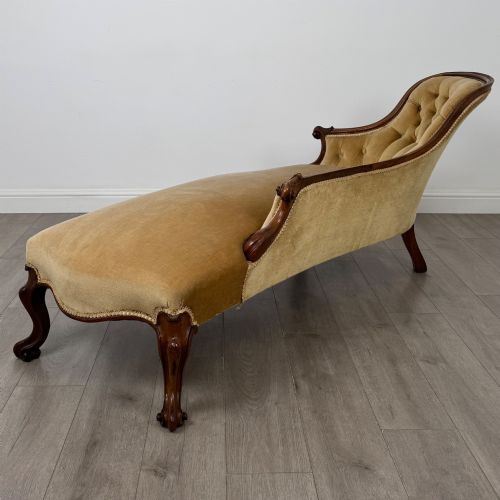 fig 3. A Victorian mahogany chaise longue featuring ochre velvet button-backed upholstery, carved trim, and cabriole legs.