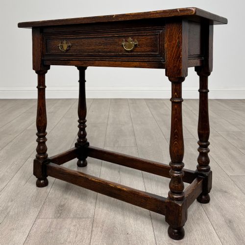 fig 1. A dark oak side table featuring a single drawer with brass drop handles, turned legs, and a perimeter box stretcher.