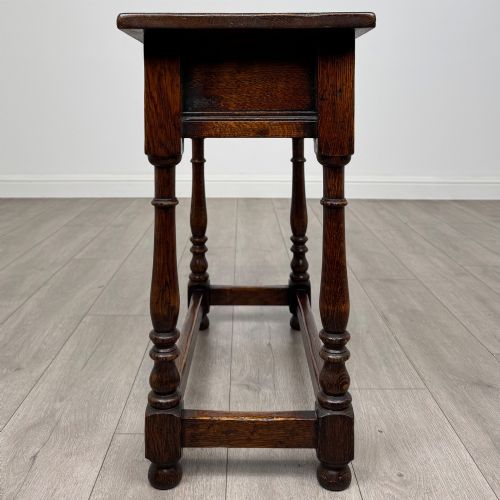 fig 2. A dark oak side table featuring a single drawer with brass drop handles, turned legs, and a perimeter box stretcher.