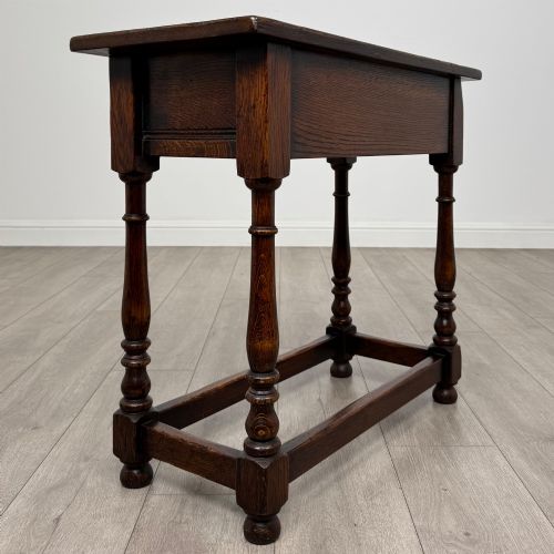 fig 3. A dark oak side table featuring a single drawer with brass drop handles, turned legs, and a perimeter box stretcher.