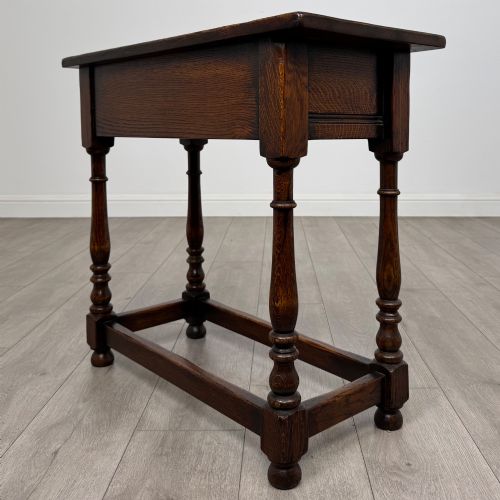 fig 5. A dark oak side table featuring a single drawer with brass drop handles, turned legs, and a perimeter box stretcher.
