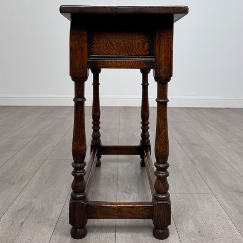 fig 6. A dark oak side table featuring a single drawer with brass drop handles, turned legs, and a perimeter box stretcher.