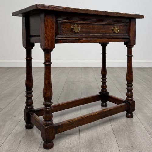 fig 7. A dark oak side table featuring a single drawer with brass drop handles, turned legs, and a perimeter box stretcher.