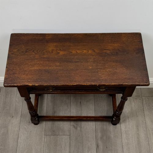 fig 8. A dark oak side table featuring a single drawer with brass drop handles, turned legs, and a perimeter box stretcher.