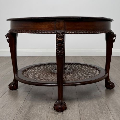 fig 1. A circular dark mahogany coffee table featuring carved lion heads atop cabriole legs ending in claw and ball feet, with a woven cane lower shelf.